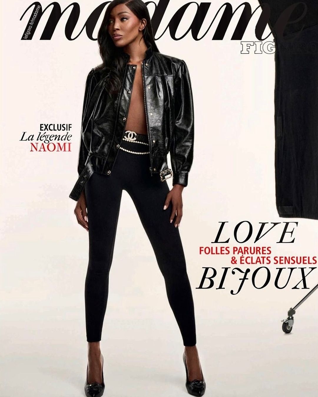 Fashion editorial shot of an adult woman with long dark hair wearing a black jacket and leggings, posing against a neutral backdrop.