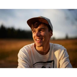 A smiling young man wearing a baseball cap and a white t-shirt outdoors at sunset captured by photographer Joseph Ford.