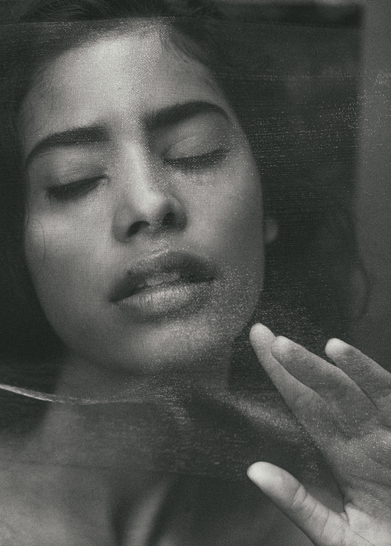 Monochrome portrait of a woman with closed eyes, facing upwards, and a hand near her face, creating a dreamlike or introspective mood.