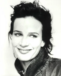 Black and white portrait of a woman with dark short hair smiling in a denim jacket against a plain background