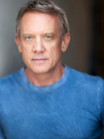 Portrait of a mature man with blue eyes wearing a blue crew-neck t-shirt against a neutral background.