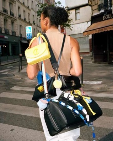 Model carrying multiple black and yellow handbags walking down a Parisian street by Joseph Molines