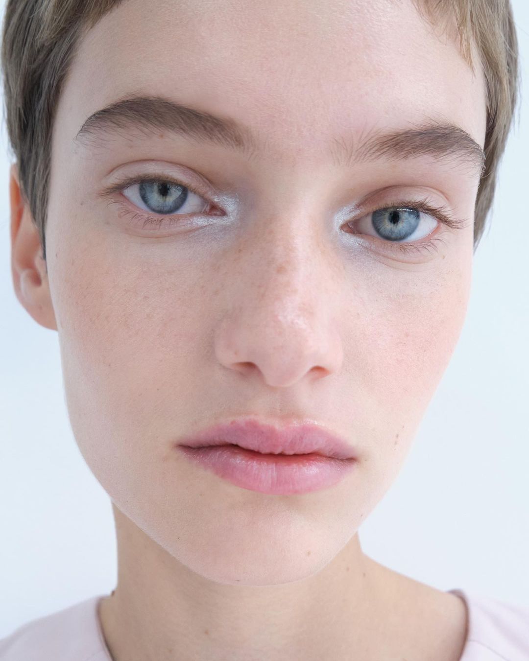 Close-up portrait of a young adult female model with fair skin, light hair, and blue eyes, in a brightly lit indoor photo studio.