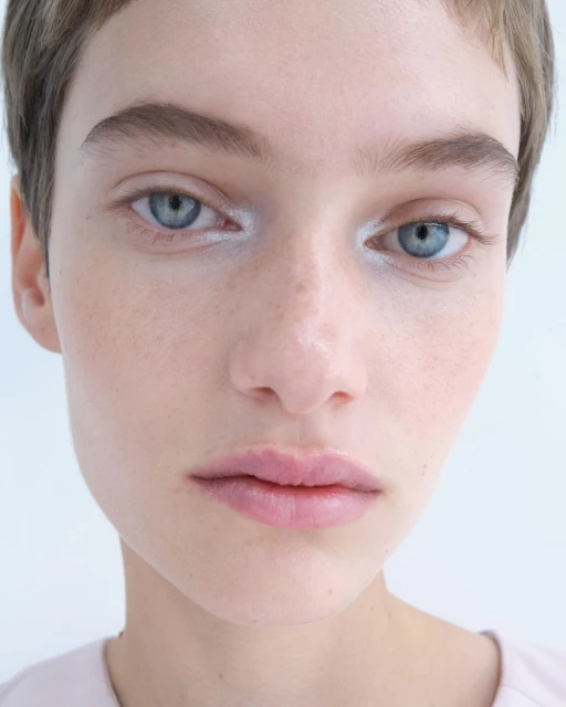 Close-up portrait of a young adult female model with fair skin, light hair, and blue eyes, in a brightly lit indoor photo studio.