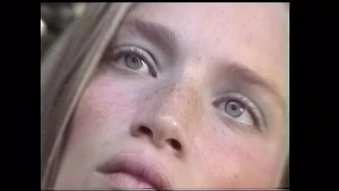 Close up portrait of a young female model with light eyes and freckles looking upwards in natural light.
