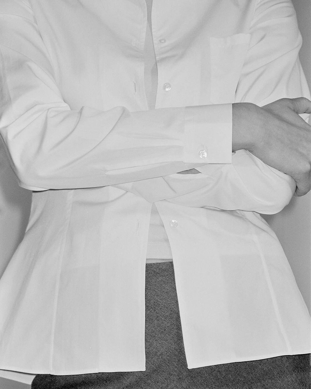 Close-up of a person in a white dress shirt with arms crossed, showing the torso and shirt detail in a monochromatic style.