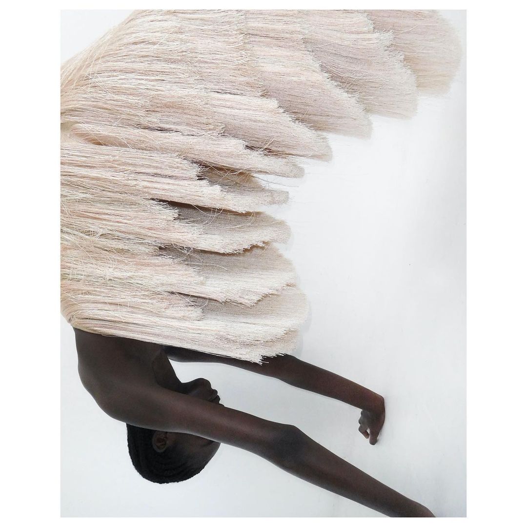 Artistic studio portrait of a slender, dark-skinned person beneath layered off-white material, creating an abstract fashion or fine-art aesthetic.