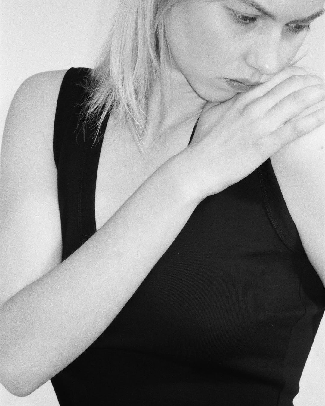 Black and white portrait of a young adult woman with light hair. She is wearing a black tank top with her arm on her shoulder.