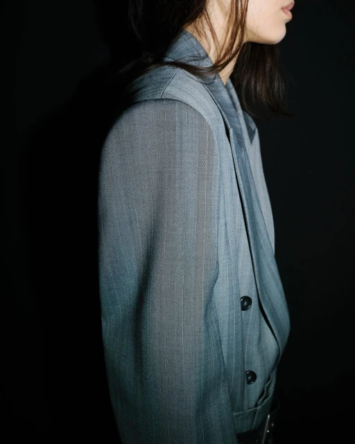 Fashion shot of a person wearing a gray herringbone suit jacket against a black background in a studio setting, providing a stylish and elegant feel.