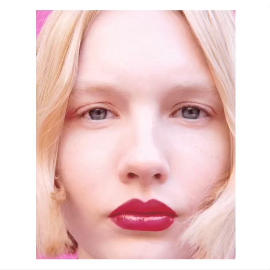 Close-up portrait of a blonde woman with red lipstick against a pink background, beauty shot, makeup focus, clean studio aesthetic.