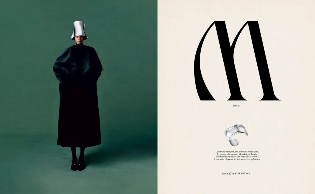 Fashion shot: Woman in long black coat and silver hat stands against dark green backdrop next to graphic typography and jewelry.