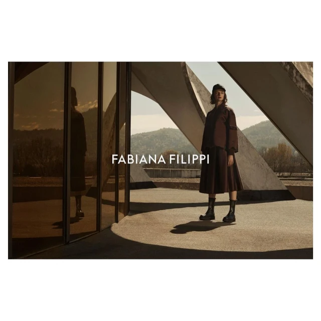 Woman in brown dress and boots posing outdoors near modern architecture; fashion editorial shot for Fabiana Filippi. Autumnal tones.