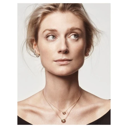 Close-up portrait of a woman wearing delicate gold layered necklaces and earrings against a plain white background