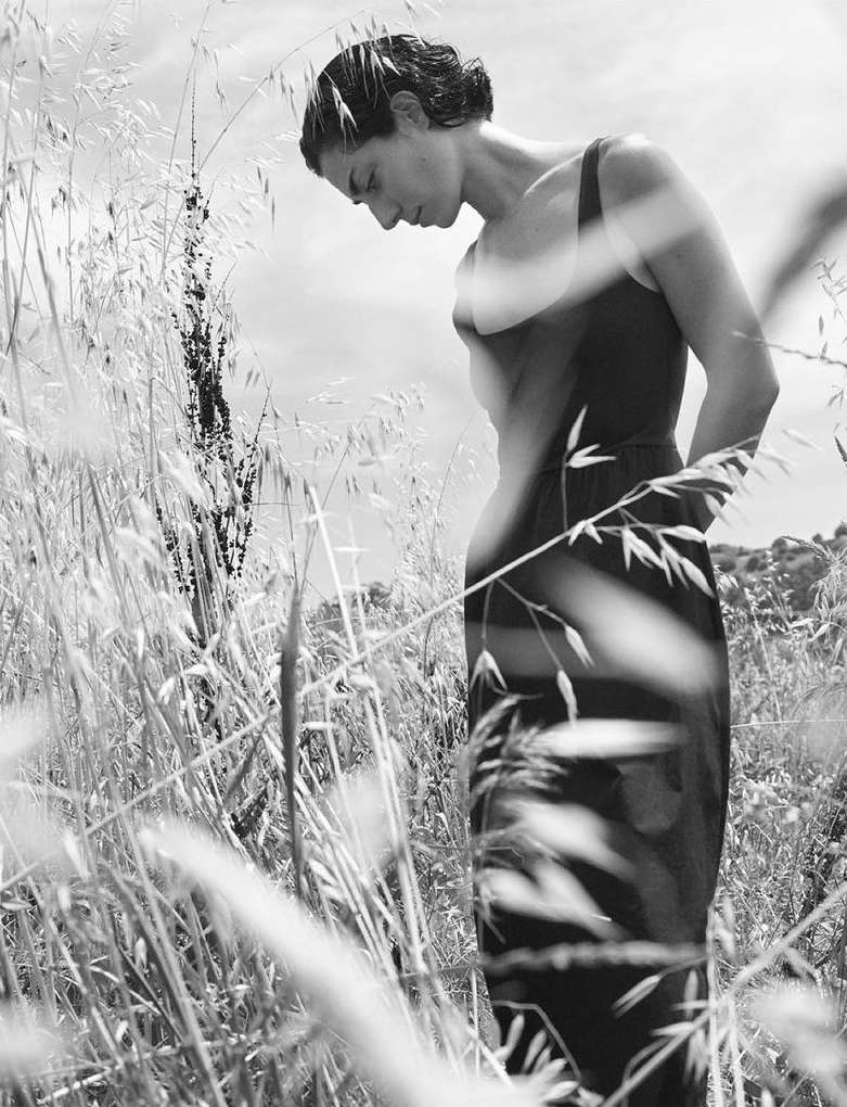 Black and white portrait of a woman standing among tall grass and wildflowers outdoors