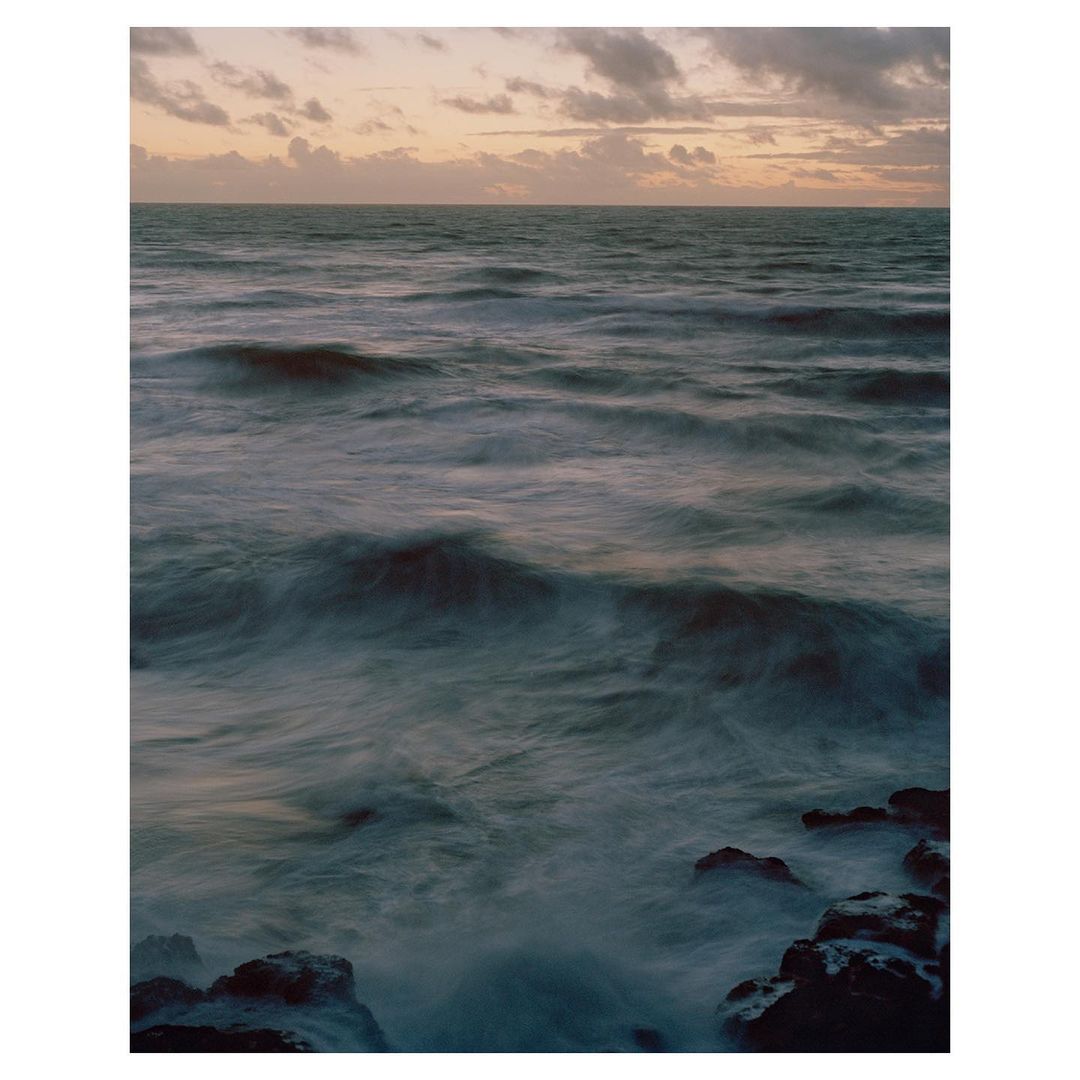 Ocean waves crashing against rocks under a cloudy sky, captured with a long exposure to create a blurred water effect.