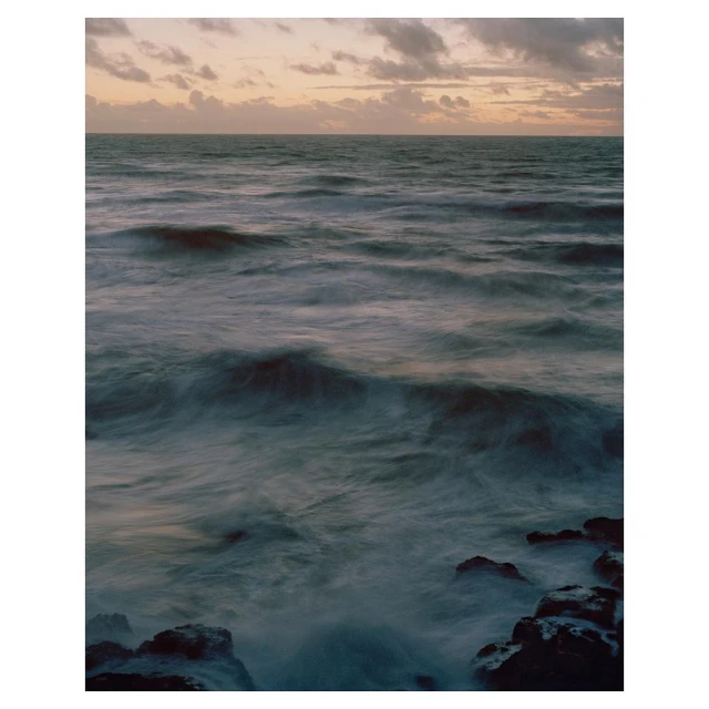 Ocean waves crashing against rocks under a cloudy sky, captured with a long exposure to create a blurred water effect.