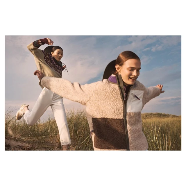 Two women wearing stylish jackets pose outdoors in a grassy field under a partly cloudy sky, showcasing fall fashion trends.