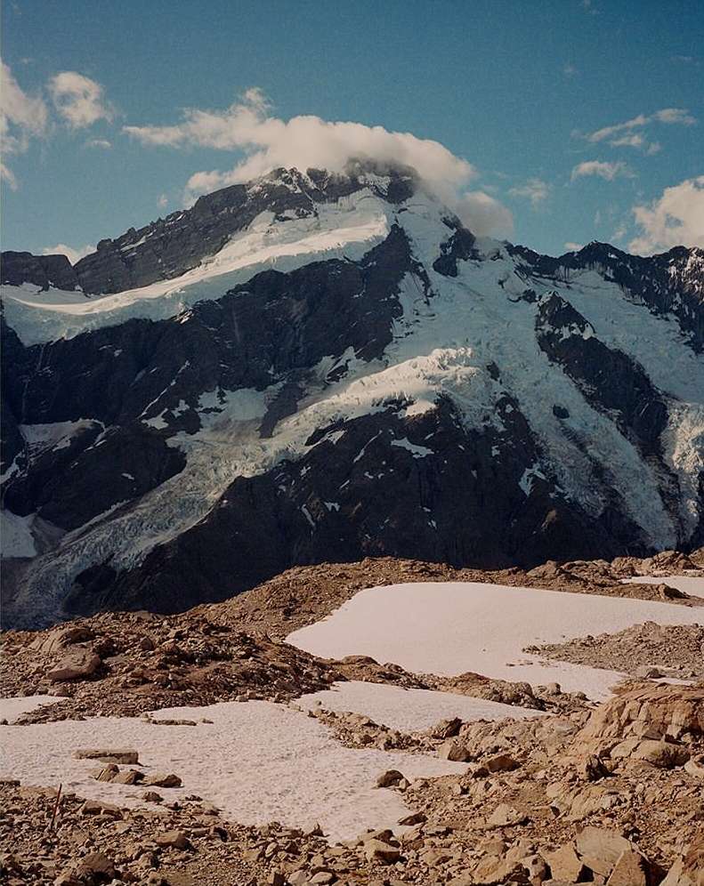 Snow-covered mountain range under a blue sky with white clouds on the summit in a scenic outdoor environment. Mountain landscape.