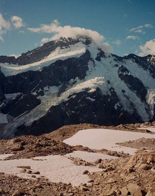 Snow-covered mountain range under a blue sky with white clouds on the summit in a scenic outdoor environment. Mountain landscape.