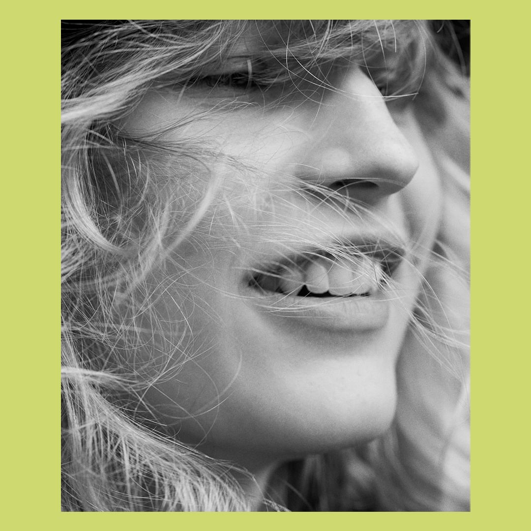 Close-up black and white portrait of a smiling woman with blowing hair framed by a chartreuse border