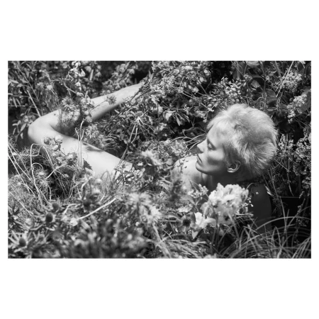Black and white portrait of a woman reclining amidst dense garden foliage and wildflowers, captured by Josh Olins.