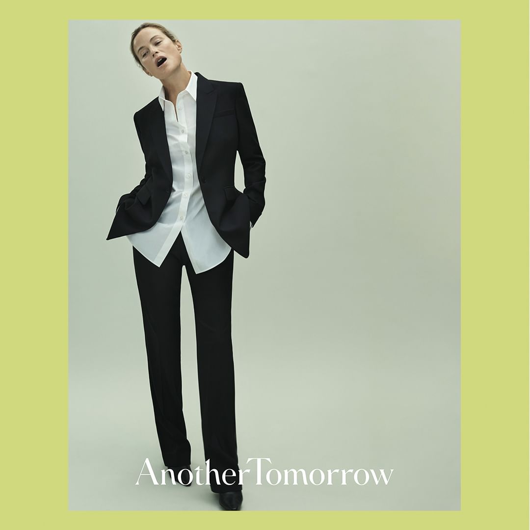 An adult female model poses in a black suit with a white shirt in a studio setting, promoting 'Another Tomorrow'.