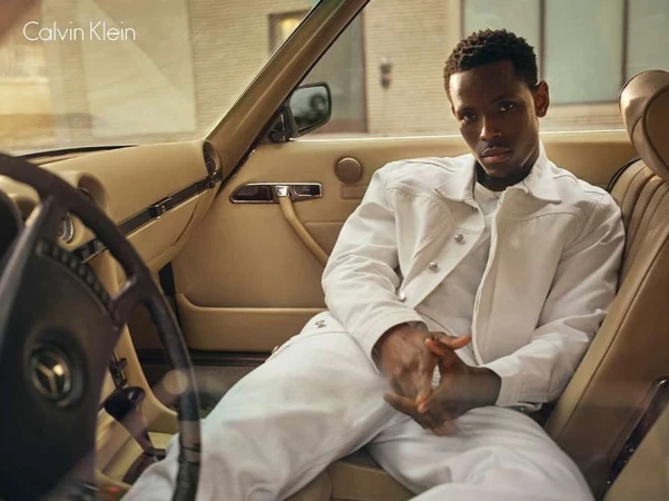 Black man wearing a white jacket and pants seated inside a vintage car with tan leather interior by photographer Josh Olins.