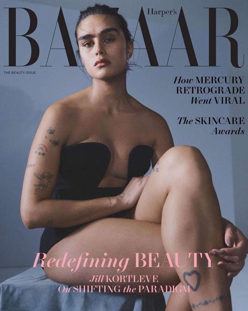 Magazine cover featuring a woman with tattoos and a black outfit sitting on a stool against a gray background. 'BAZAAR' in bold at top.