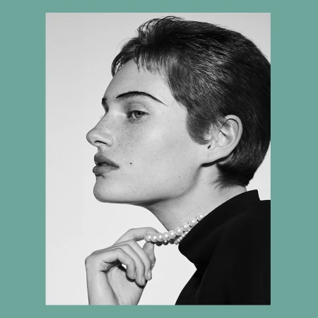 Black and white profile portrait of a woman with short hair wearing a pearl necklace and dark top by Josh Olins