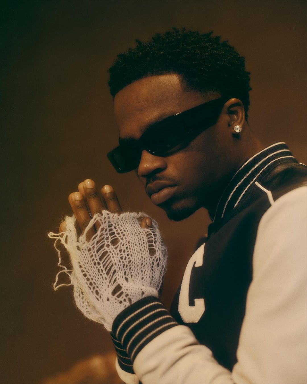 Close-up of a stylish African-American man wearing black sunglasses and letterman jacket in a portrait with soft lighting.