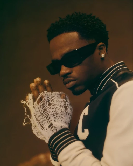 Close-up of a stylish African-American man wearing black sunglasses and letterman jacket in a portrait with soft lighting.