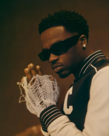 Close-up of a stylish African-American man wearing black sunglasses and letterman jacket in a portrait with soft lighting.