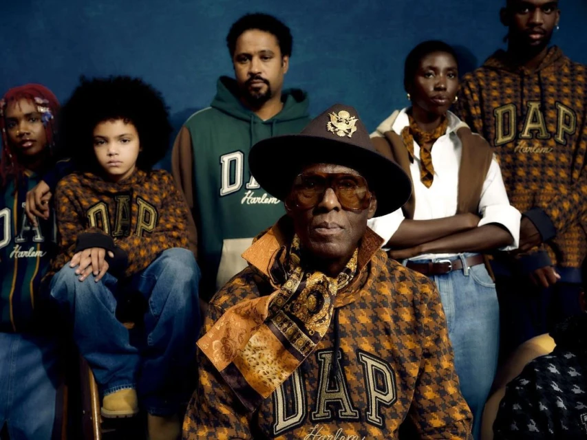 Group portrait of six people wearing apparel with 'DAP Harlem' emblem, set against a blue backdrop in a studio setting.