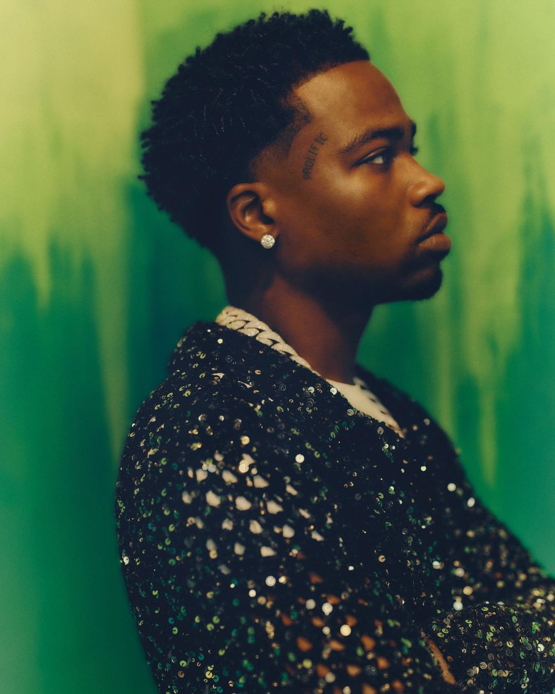 Portrait of a Black man in a dark sequin jacket against a green gradient background by photographer Joshua Kissi.