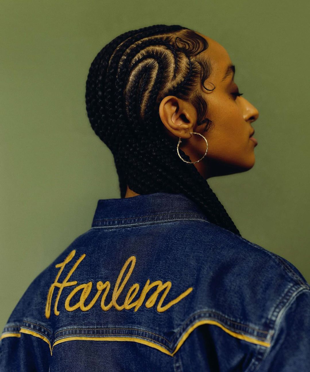 Profile of a young adult woman with braided hair, wearing a denim jacket with the word "Harlem" embroidered on the back.