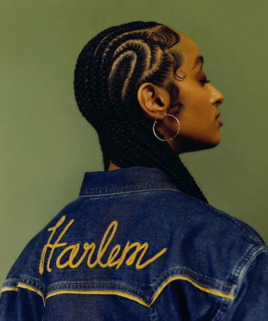 Profile of a young adult woman with braided hair, wearing a denim jacket with the word "Harlem" embroidered on the back.