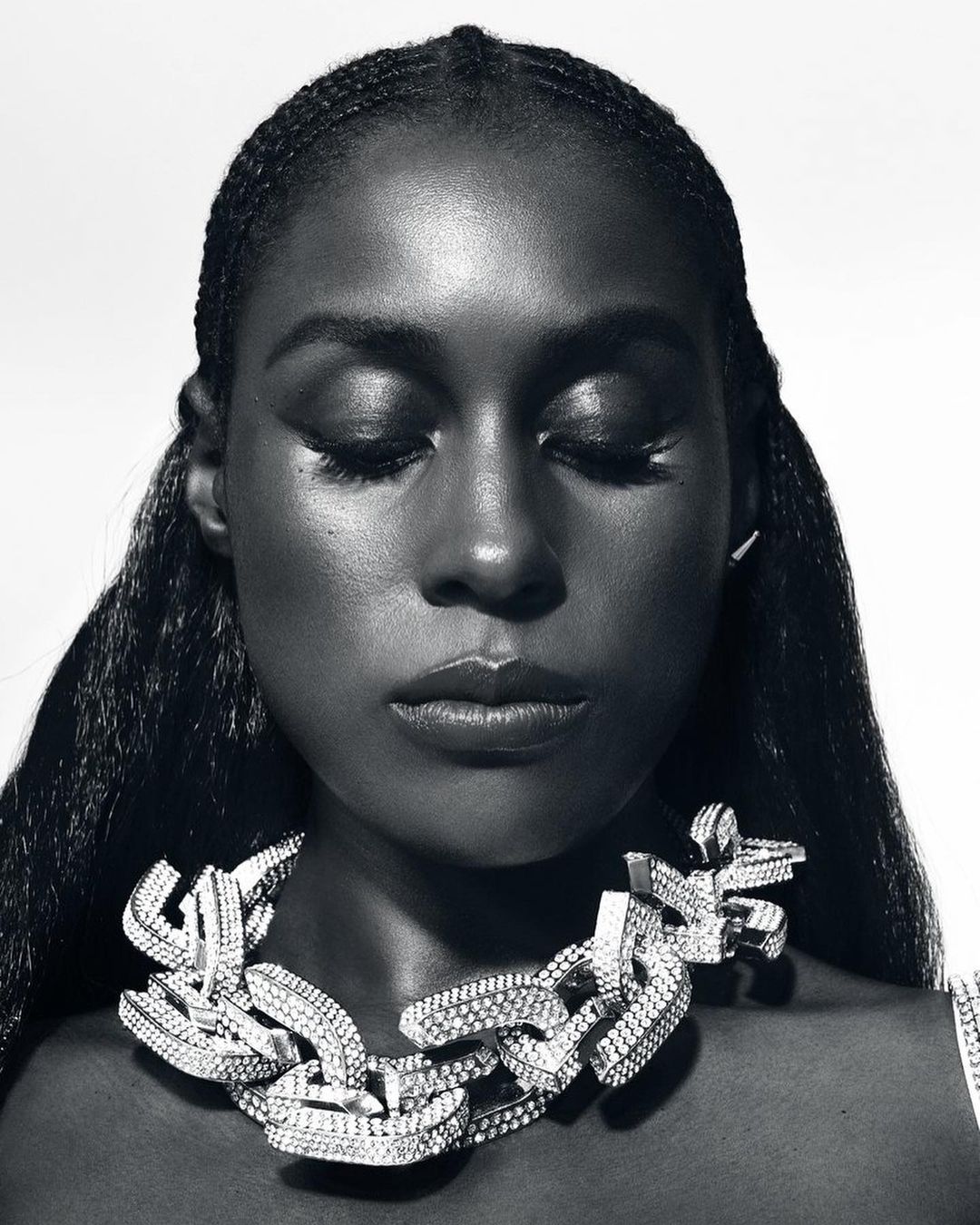 Monochrome portrait of a Black woman with closed eyes wearing a large diamond chain necklace against a white background.