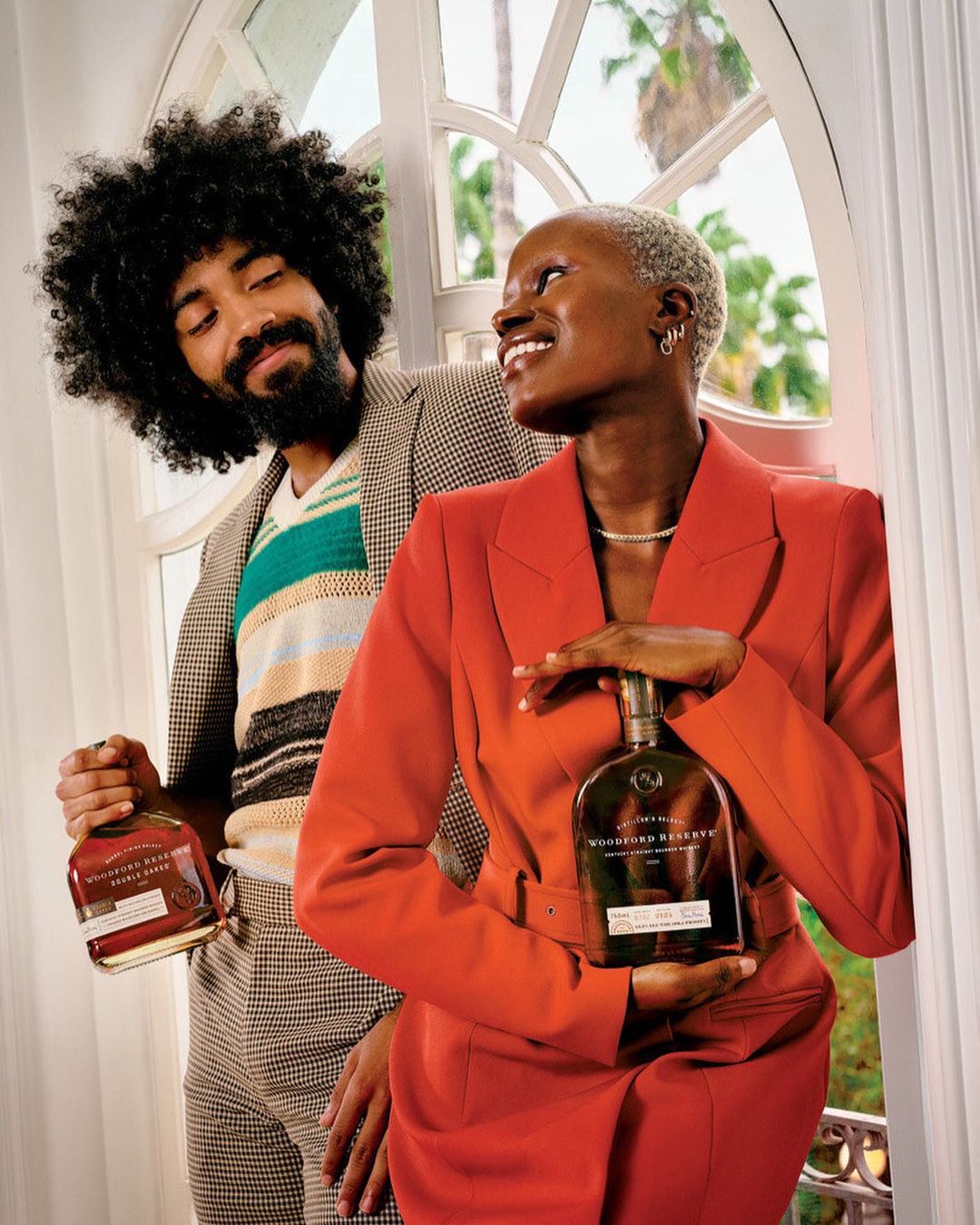 Two models holding liquor bottles by arched window, photographed by Joshua Kissi