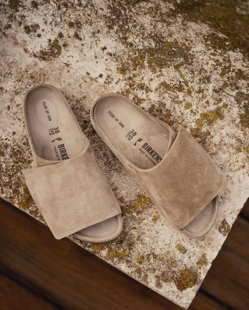Neutral tone photo featuring a pair of suede Birkenstock clogs on a textured concrete surface, showcasing minimalist footwear design.