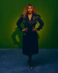 Serena Williams posing in a black trench coat against a deep green and blue studio backdrop photographed by Joshua Kissi.