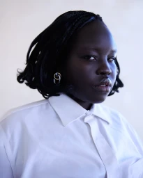 Close-up portrait of a Black woman with short braided hair wearing a white collared shirt and interlocking hoop earrings.