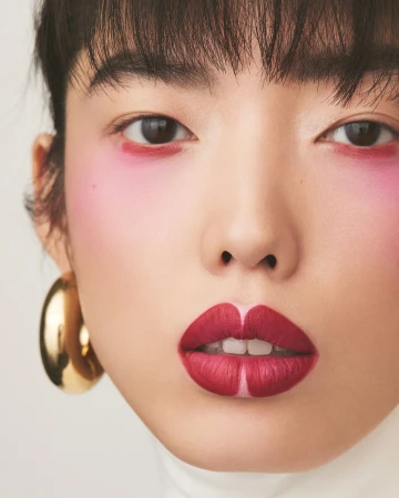 Close up beauty portrait of a model with bold pink eye makeup, deep red lipstick, and large gold hoop earrings by Joshua Pestka