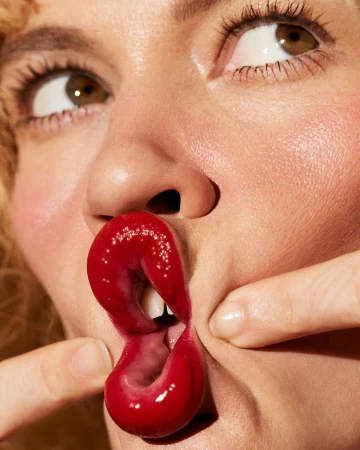 Close-up portrait of a woman pulling her lips with her fingers, wearing glossy red lipstick