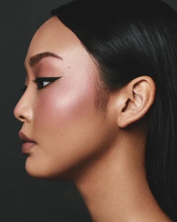 Side profile of a beautiful Asian woman with black hair and soft, glamorous makeup, set against a dark gray background in a beauty portrait.