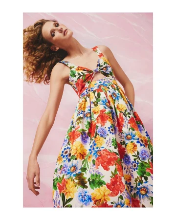 Model with long curly brown hair wearing a colourful floral print dress against a pink backdrop, photographed by Joshua Pestka