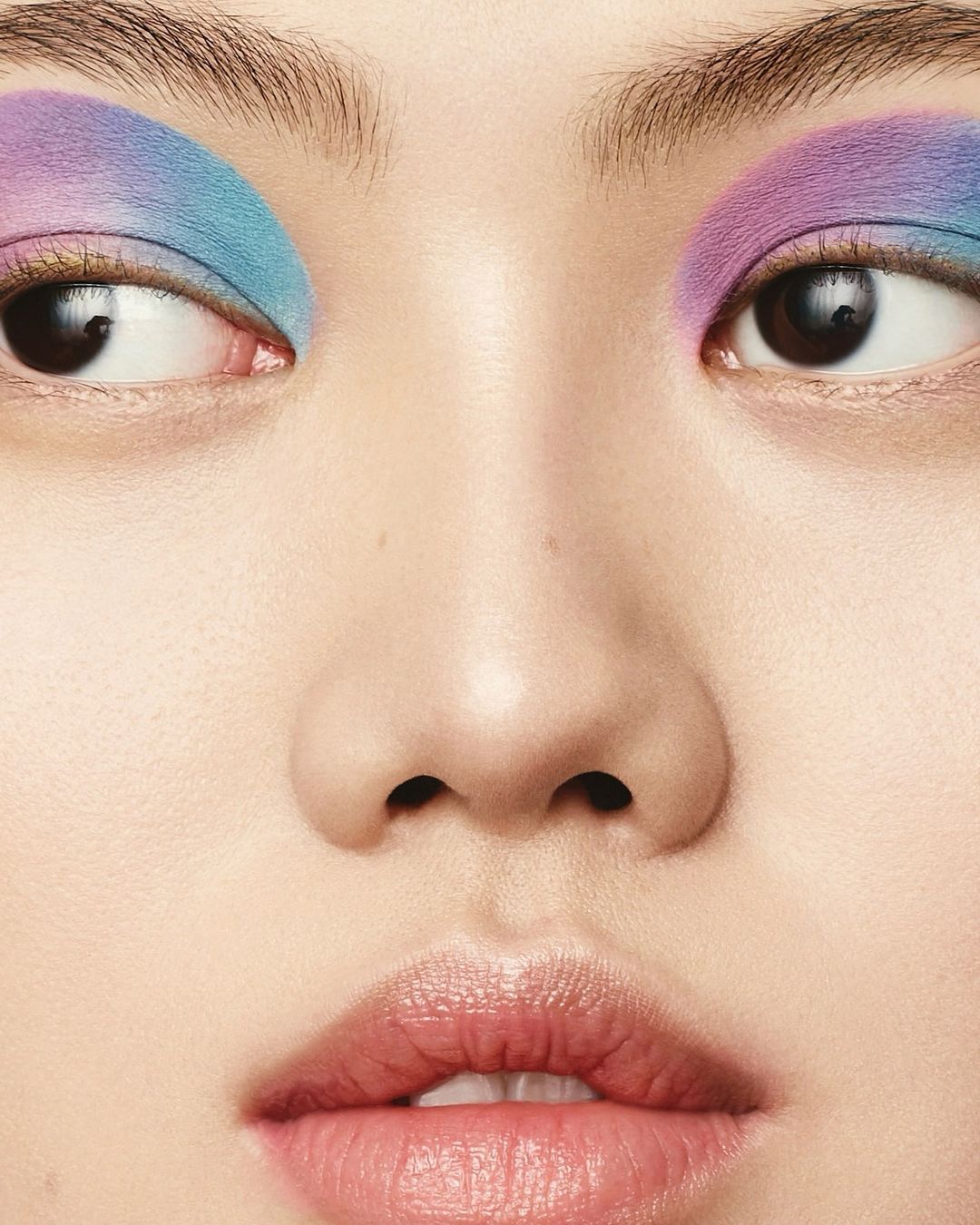 Close-up of a woman's face featuring vibrant blue and purple eyeshadow, highlighting the eye makeup in a beauty and fashion context.