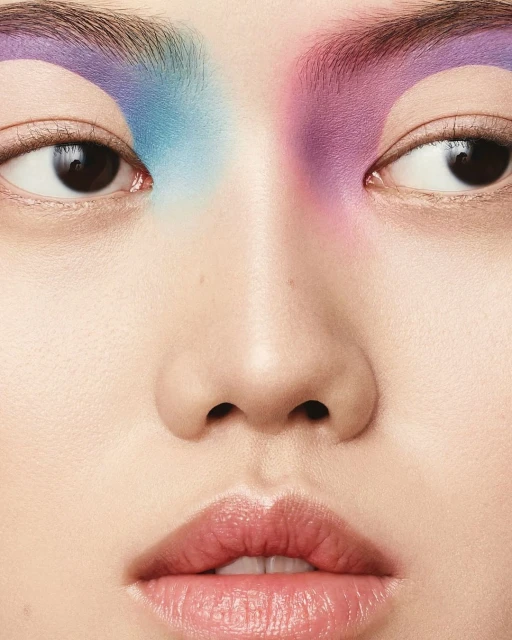 Close-up portrait of a woman with creative eyebrow makeup in shades of blue and purple, showcasing the artistic beauty look.
