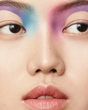 Close-up portrait of a woman with creative eyebrow makeup in shades of blue and purple, showcasing the artistic beauty look.
