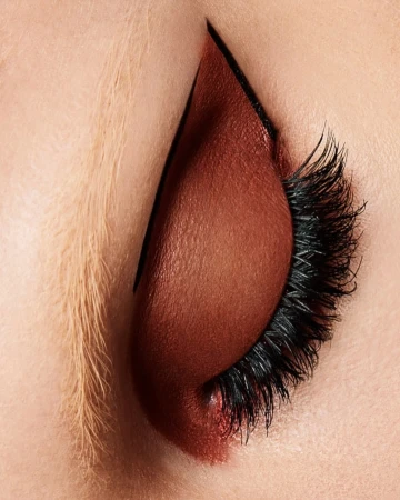 Close-up studio shot of an adult female face with brown makeup on eyelid and long black eyelashes, skin details, and blonde eyebrow.