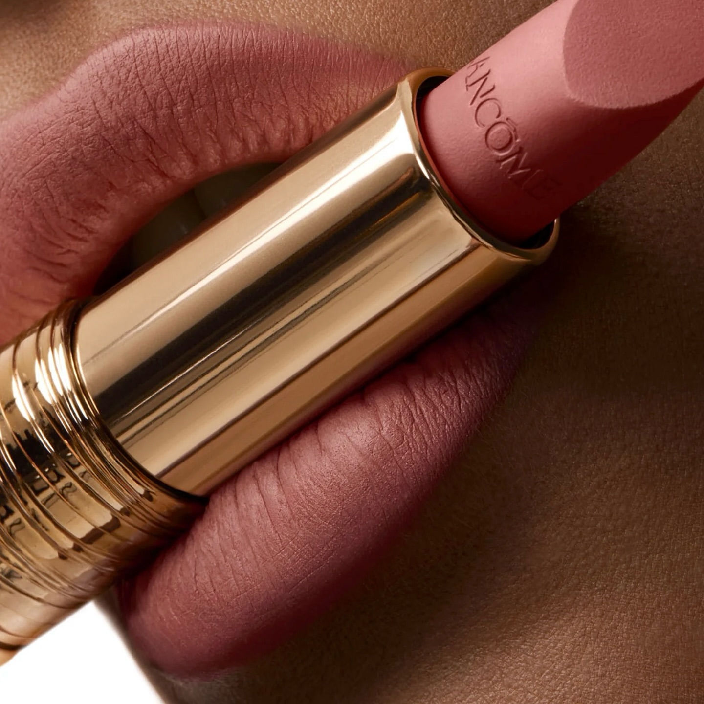 Close-up of pink lipstick by Lancome against skin. Gold tube with brand name visible. Beauty and cosmetics shot with macro details.